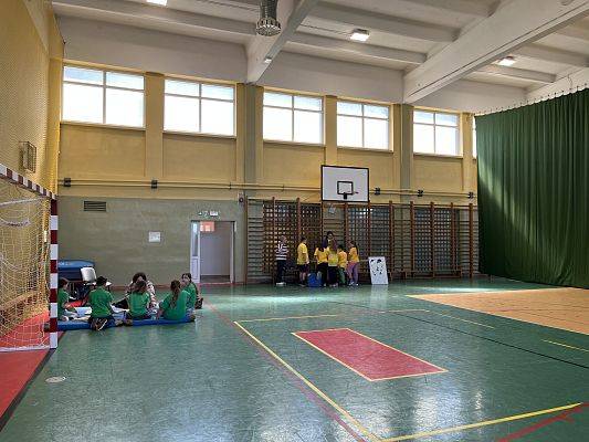 sala gimnastyczna na niej dwie grupi dzieci skupione przy dwóch różnych stoiskach edukacyjnych
