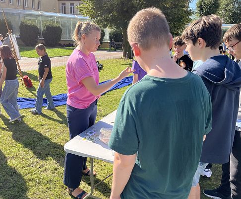 grupa młodzieży przy stole, w centralnym punkcie kobieta, która pokazuje coś palcem z surową miną.