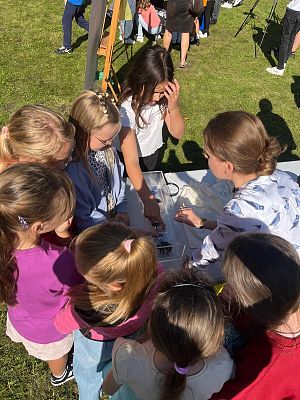 grupa dzieci wokół stołu na którym stoi gablotka z modelami owadów. zdjecie zrobione na podwórku.