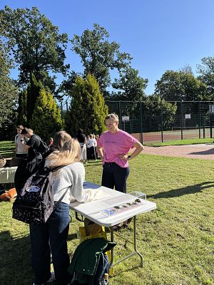 przy stole postawionym przy boisku szkolnym dwie osoby wkładają ręce do woreczków.