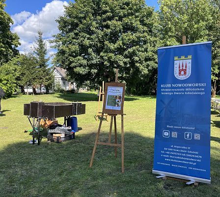 widok na sztalugę z plakatem o pikniku bioróżnorodności oraz rollup Klubu Nowodworskiego