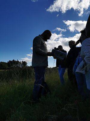 mężczyzna z dużą księżką o ptakach stosi na trawie, przed nim kilka osób.