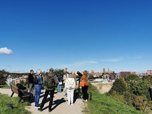 Grupa osób stoi na górce, w oddali zarys miasta.