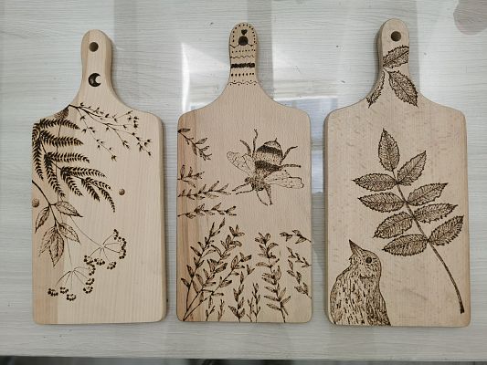 3 deski drewniane (kuchenne), każda z innym rysunkiem wypalonym pirografem. Jedna ma rysunek roślin, druga rośliny i owada, a trzecia liście i ptaka