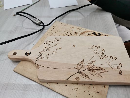 drewniana deska kuchenna ozdobiona wizerunkiem roślin, które zostały wypalone na desce pirografem.