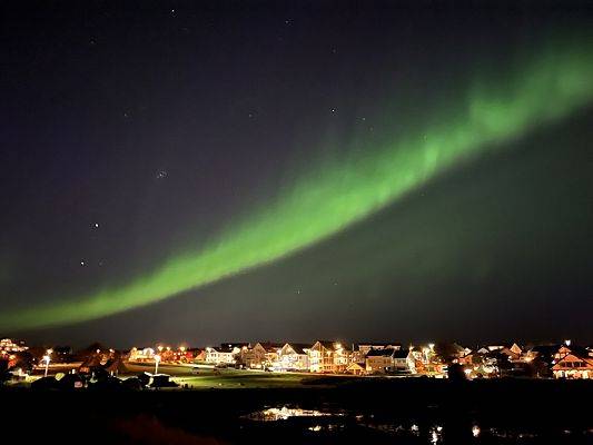 Zilona zorza polarna nad oświetlonym miasteczkiem.